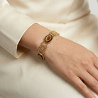 Gold bracelet with a central tortoise brown stone on a wrist against a white background
