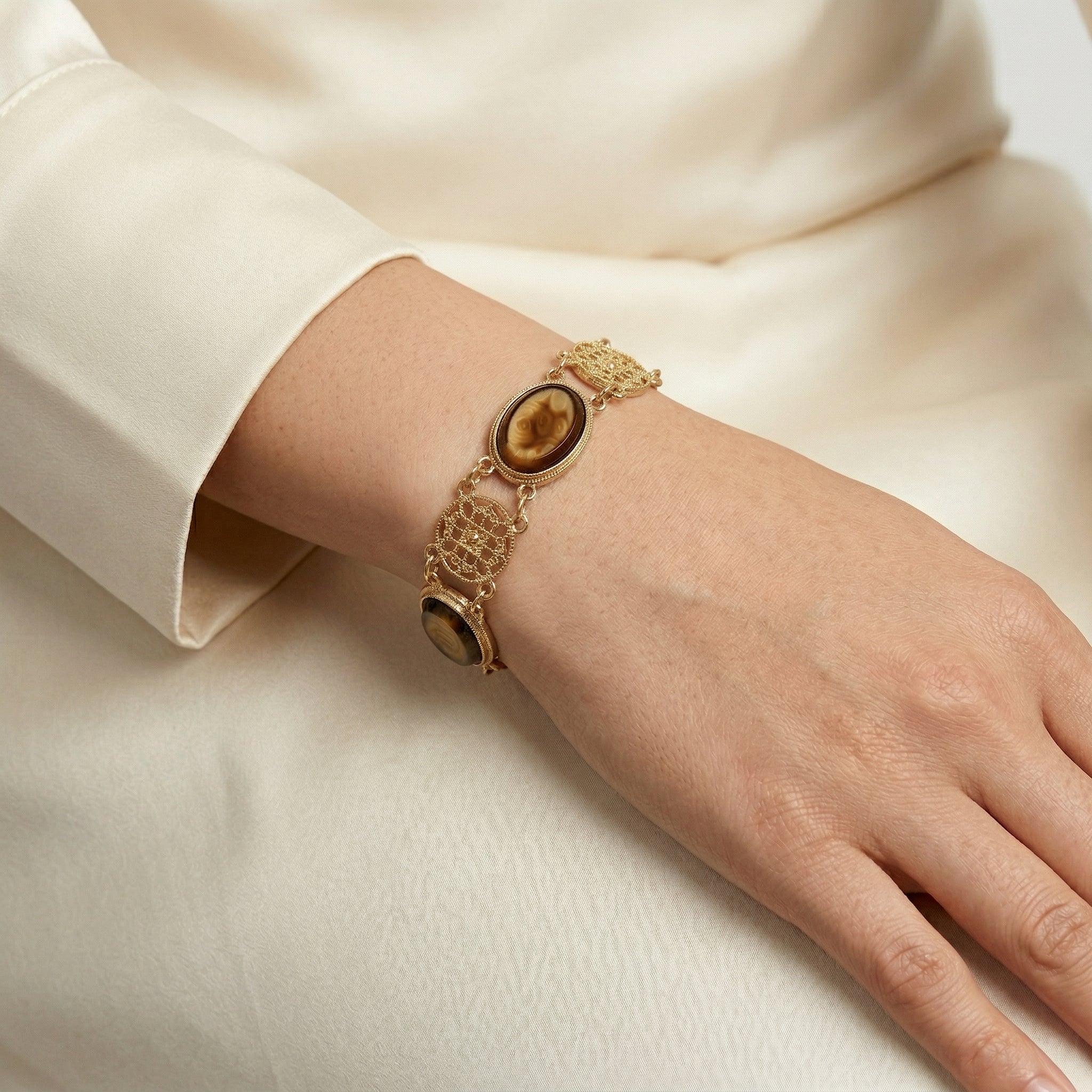 Gold bracelet with a central tortoise brown stone on a wrist against a white background