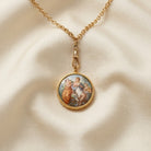 Gold necklace with a pendant featuring classical Rubenesque design on a beige fabric background