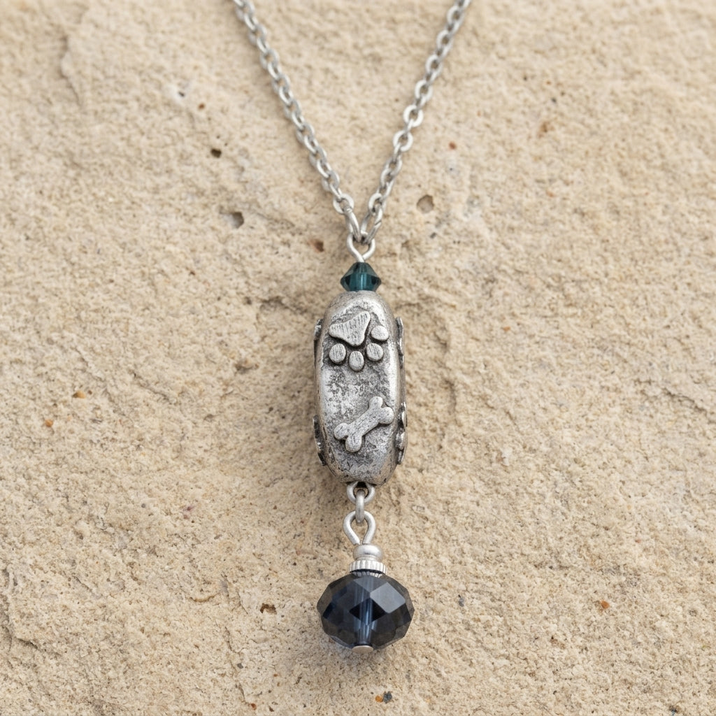 Necklace with a silver paws and bones pendant and a dangling blue crystal on a beige surface