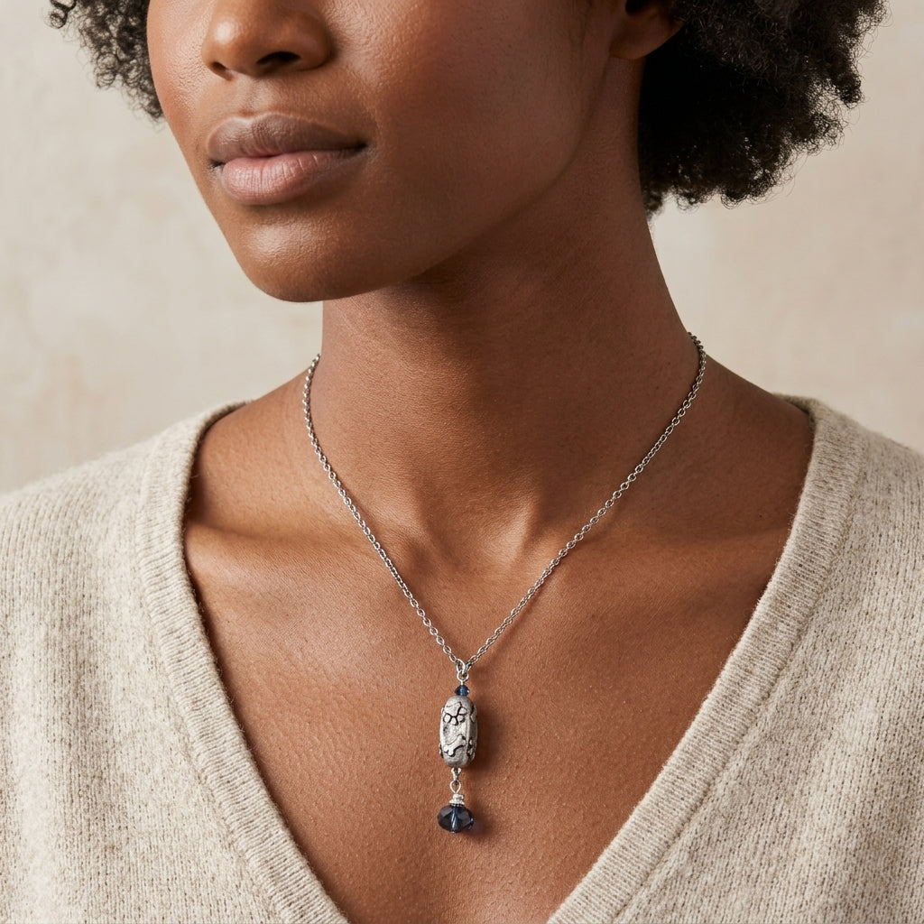 Woman wearing a necklace with a paws and bones pendant and a dangling montana blue crystal on a neutral background