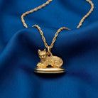 Gold cat-shaped locket pendant on a chain against a blue fabric background