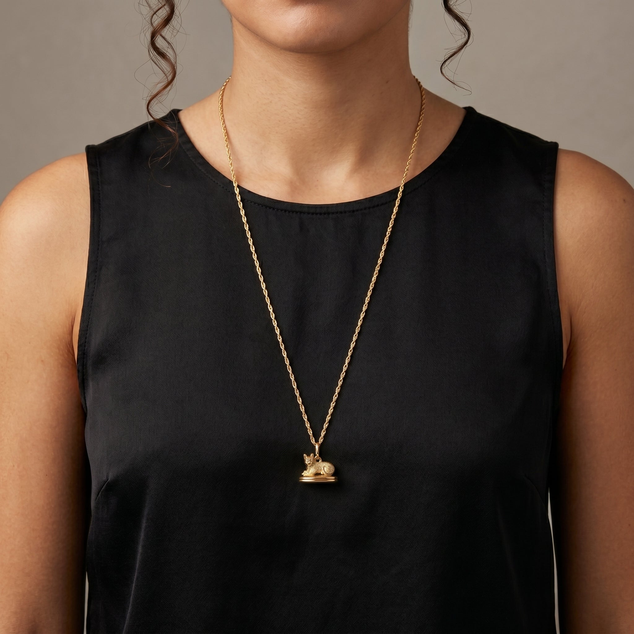 Person wearing a black sleeveless top with a gold necklace featuring a small cat locket pendant.