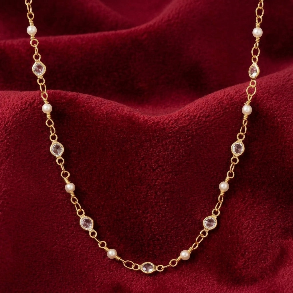 Gold tone necklace with clear crystals and white faux pearls resting on red velvet fabric