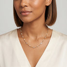 Woman wearing a white top with a gold tone necklace accented with clear crystals and white faux pearls. 