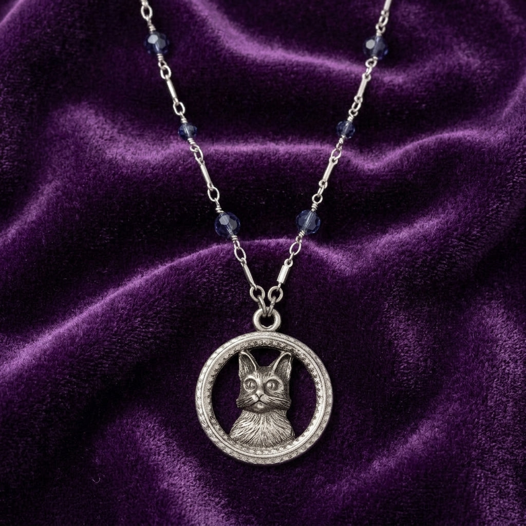 Silver necklace that has blue crystal beads with a cat pendant on a purple velvet background