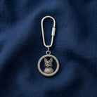 Silver keychain with a cat design on a blue fabric background