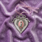 Decorative heart-shaped ornament with a cat illustration on pink enamel on a purple fabric background