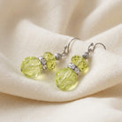 Dual Elegance Light Green Crystal Drop Earrings resting on a cream cloth surface