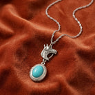 Silver horse head pendant necklace with a turquoise stone resting on dark red fabric