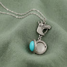 Necklace with a silver horse head pendant and turquoise stone on green fabric
