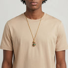 Man wearing a gold necklace with a green and red egg pendant on a plain background