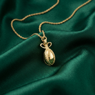 Gold necklace with an egg pendant on a green fabric background