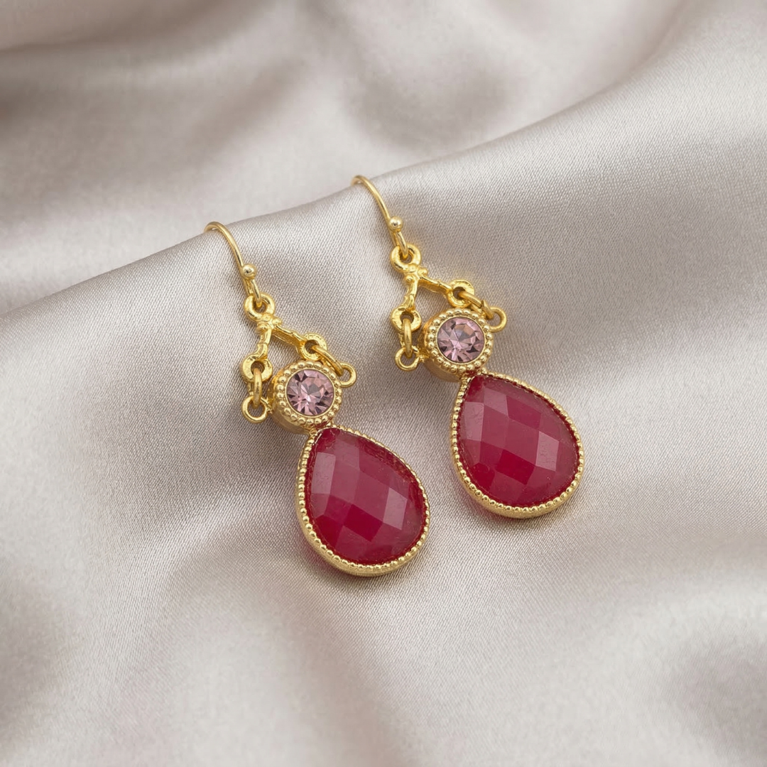 Gold earrings with red teardrop-shaped crystals on a satin surface