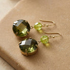Round Green Stone Dangle Earrings resting on smooth tan-colored stone