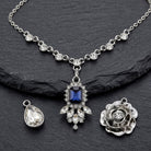 Silver tone necklace set with three different pendants and a blue crystal on a textured dark stone surface