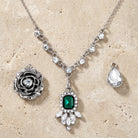 Silver tone necklace set with three different pendants and an emerald green crystal on a textured beige surface