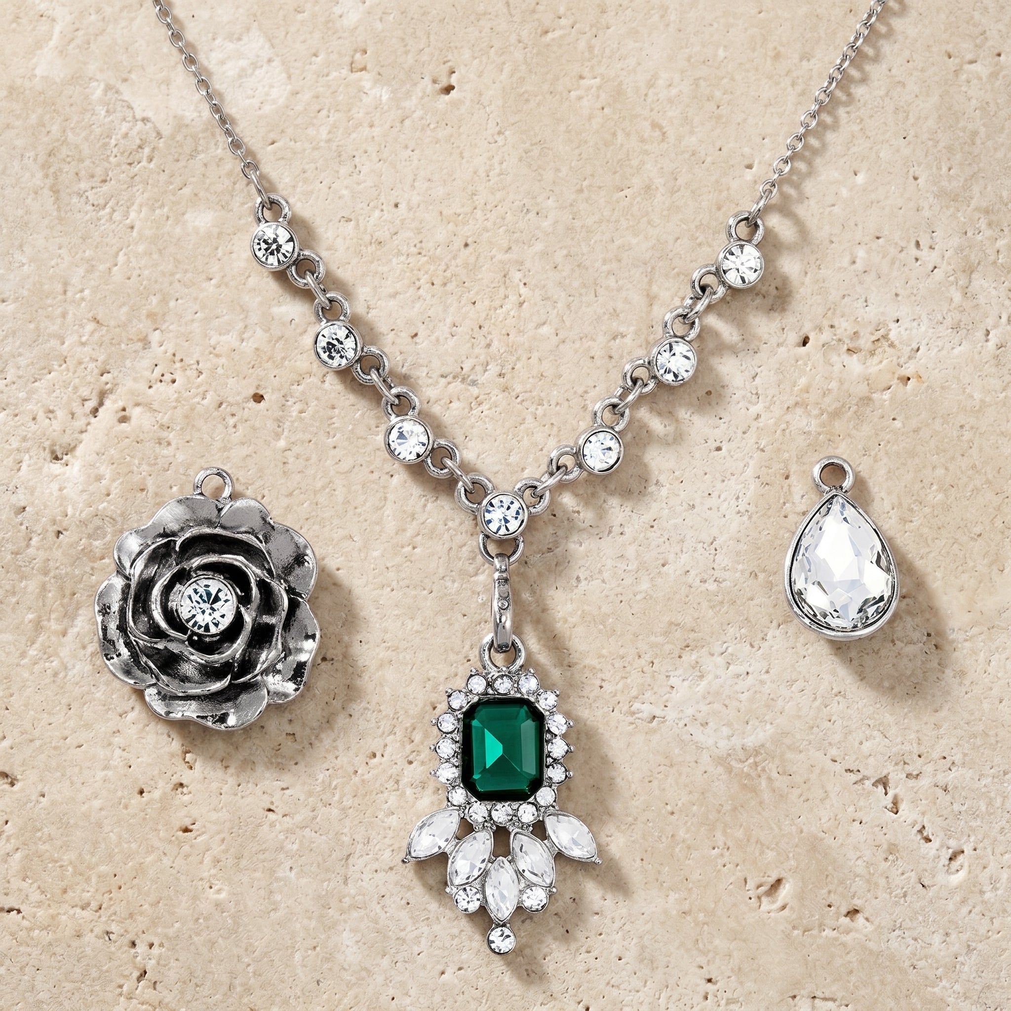 Silver tone necklace set with three different pendants and an emerald green crystal on a textured beige surface