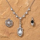 Silver tone jewelry set with three interchangeable pendant and clear and black crystals resting on light brown sandstone surface
