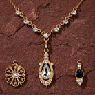 Gold tone jewelry set with three interchangeable pendant and clear and black crystals resting on dark brown sandstone surface