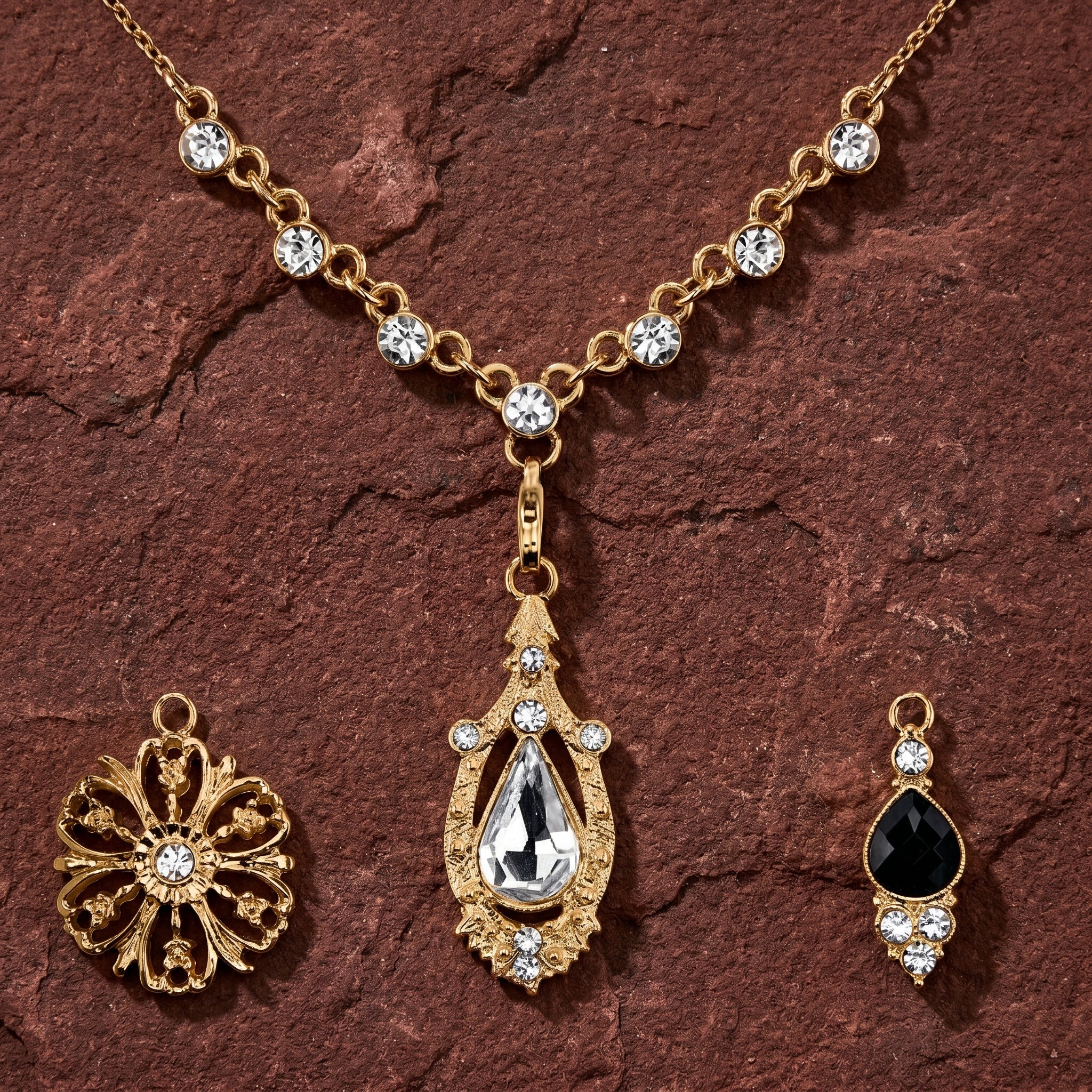 Gold tone jewelry set with three interchangeable pendant and clear and black crystals resting on dark brown sandstone surface
