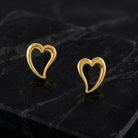 Gold Open Heart Stud Earrings resting on smooth black stone surface