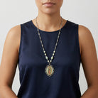Person wearing a long religious necklace with an Our Lady of Guadalupe pendant on a plain background