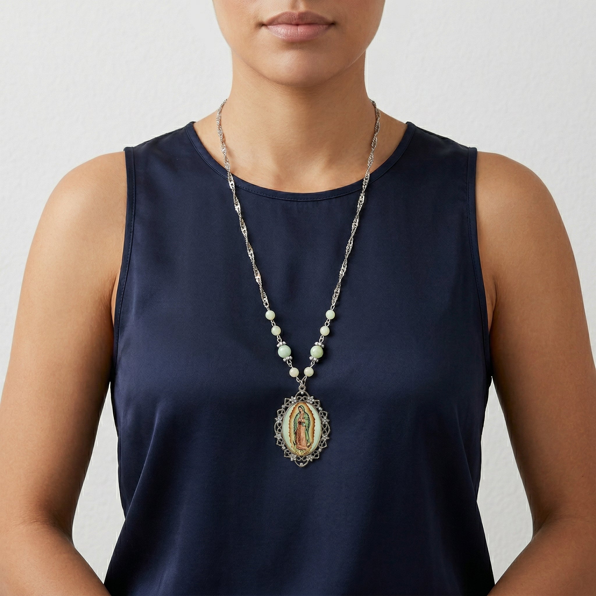 Person wearing a long religious necklace with an Our Lady of Guadalupe pendant on a plain background