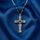 Silver floral cross necklace with blue crystals on a blue fabric background