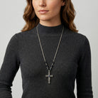 Person wearing a dark gray turtleneck sweater with a long necklace featuring a cross pendant and Montana Blue crystals.