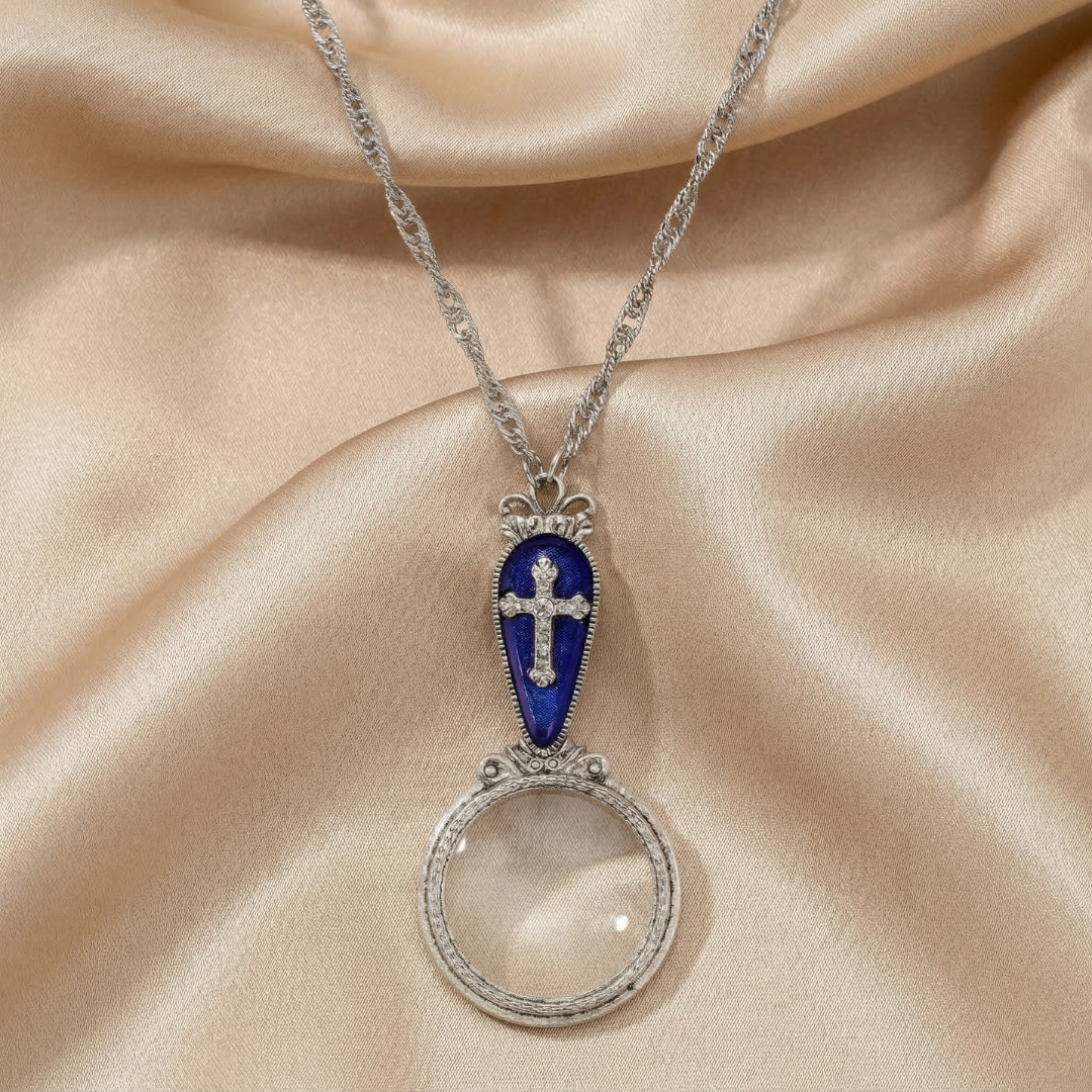 Decorative necklace with a blue magnifying glass pendant and cross on a beige fabric background