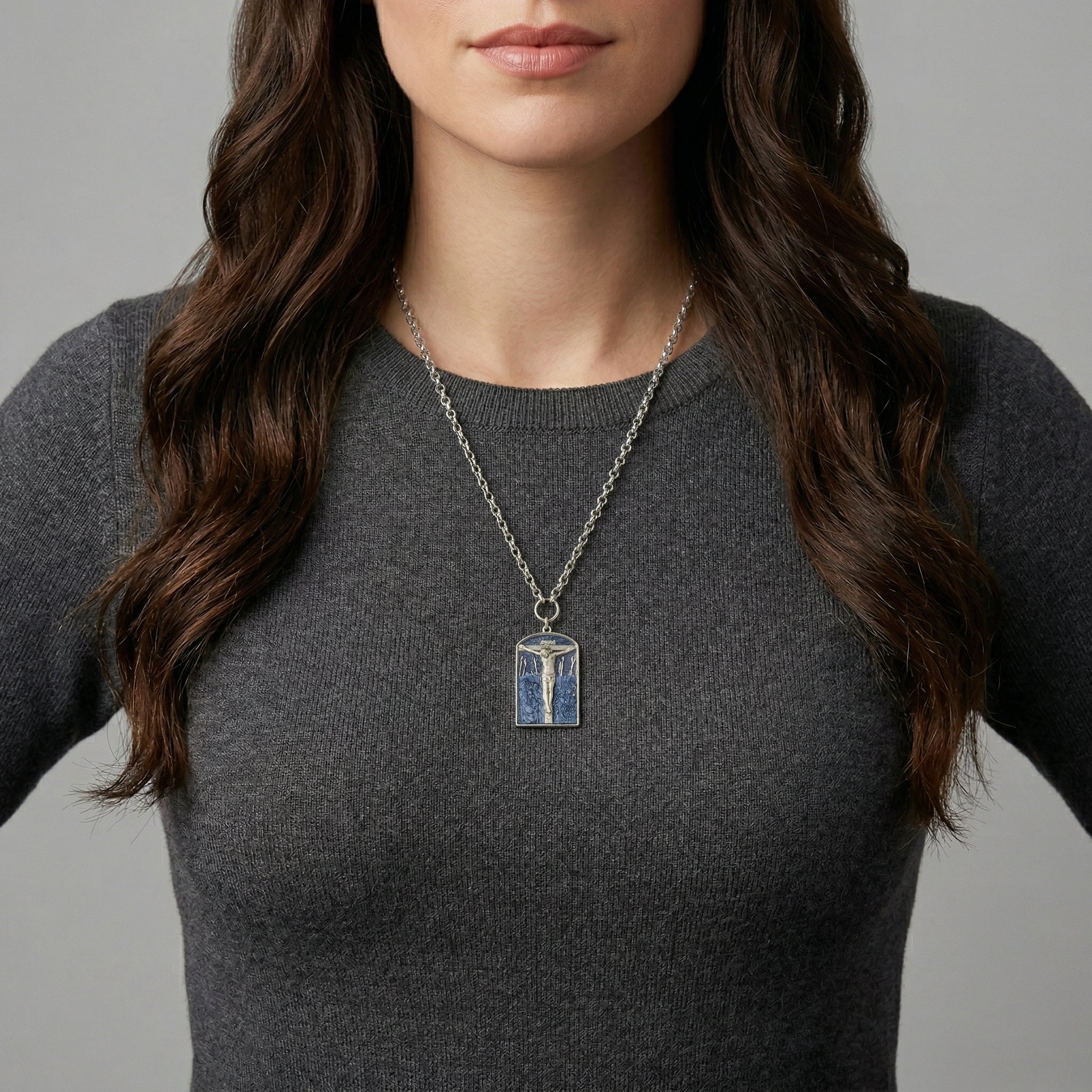 Woman wearing a necklace with a religious pendant necklace depicting the crucifixion of Jesus against a gray background