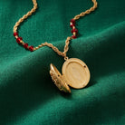 Gold opened locket necklace with red beads on a green fabric background