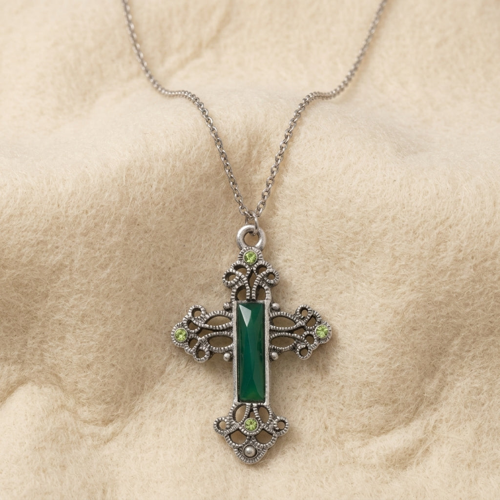 Decorative cross pendant with a green stone and crystals and a chain on beige fabric