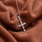 Silver cross pendant necklace with dazzling crystals on a brown fabric background