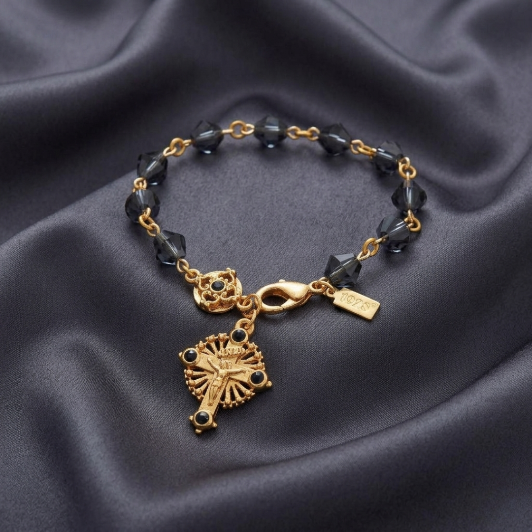 Gold crucifix bracelet with blue beads and a decorative clasp on a dark fabric background