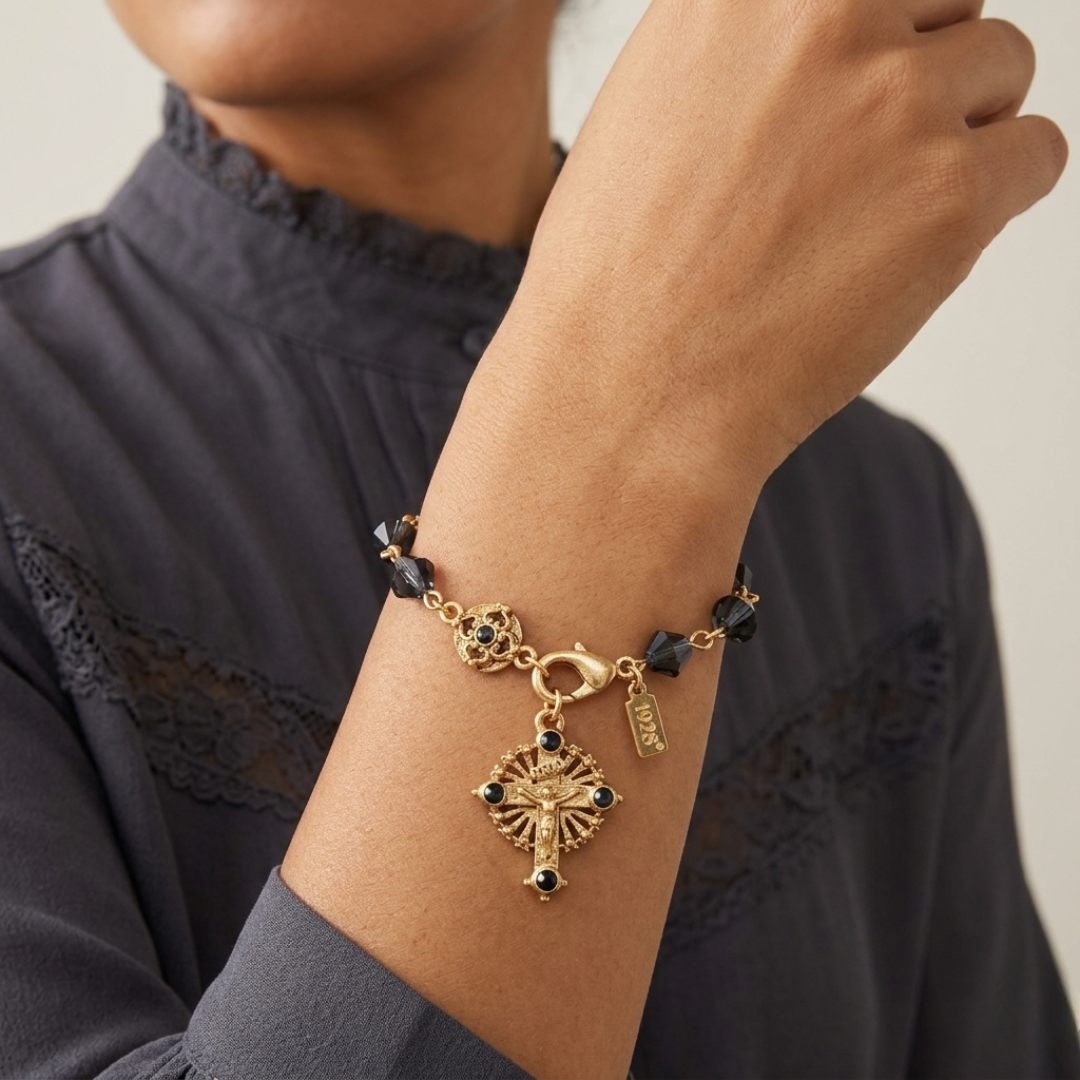 Gold-dipped bracelet with blue beads and a crucifix pendant on a wrist against a neutral background
