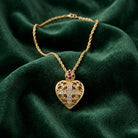 Gold heart-shaped necklace with a cross design on a green fabric background
