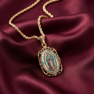 Gold necklace with a religious Lady of Guadalupe pendant on a maroon fabric background