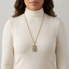 Woman wearing a gold necklace with the sacred Lady of Guadalupe pendant on a plain background