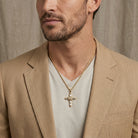 Man wearing a beige blazer and gold necklace with a cross pendant against a neutral background