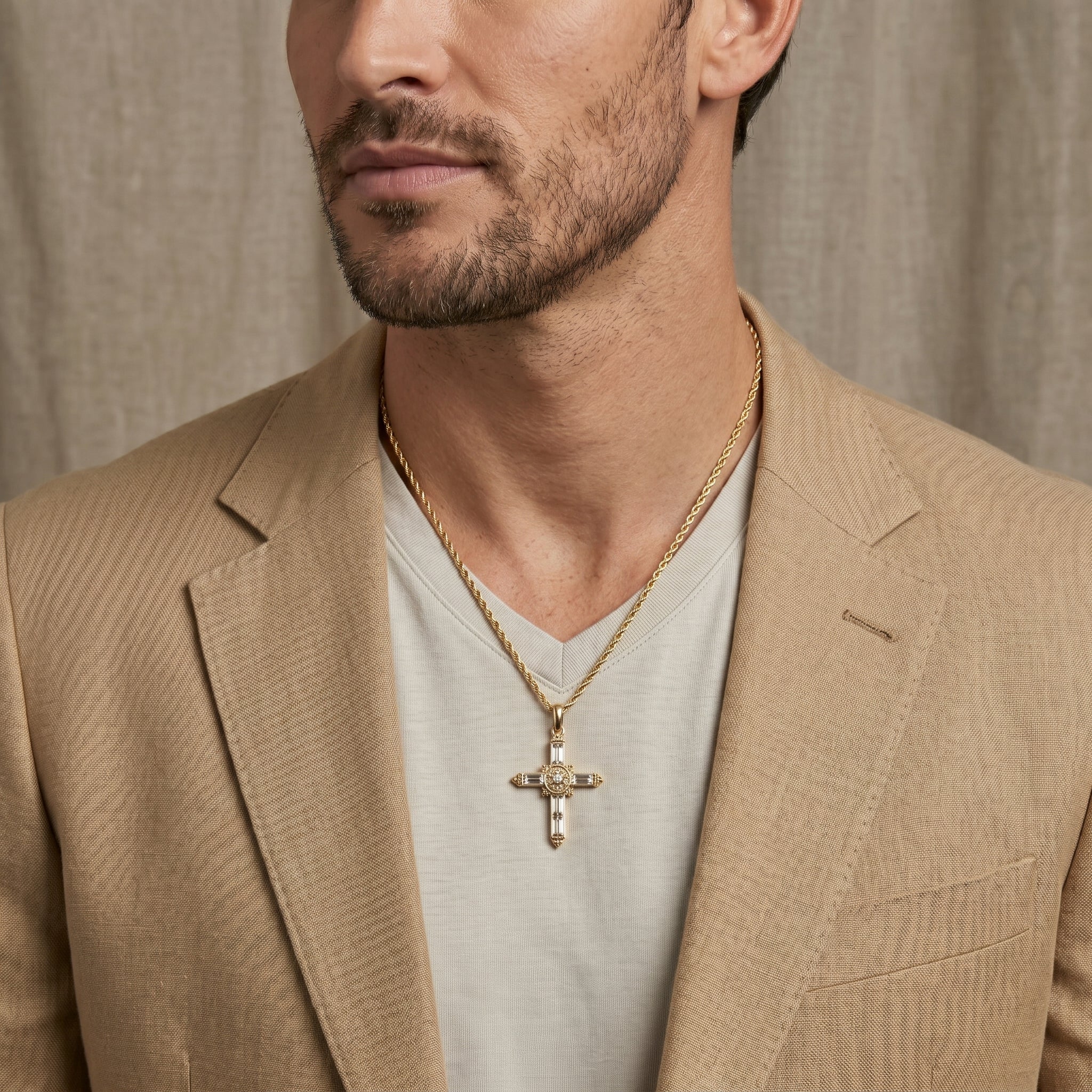 Man wearing a beige blazer and gold necklace with a cross pendant against a neutral background
