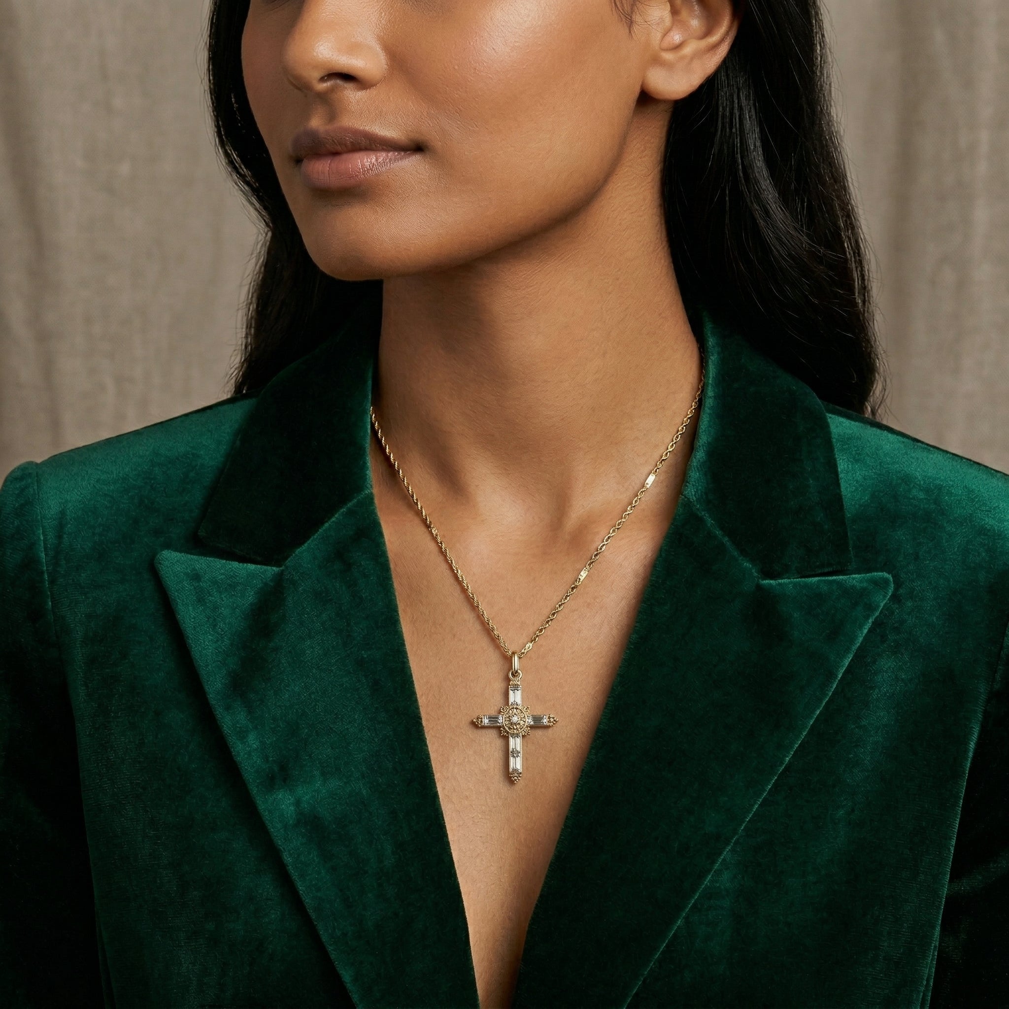 Woman wearing a gold necklace with a cross pendant that has crystal accents against a neutral background