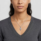 Woman wearing a silver necklace with a cross pendant and clear and blue crystals on a plain background