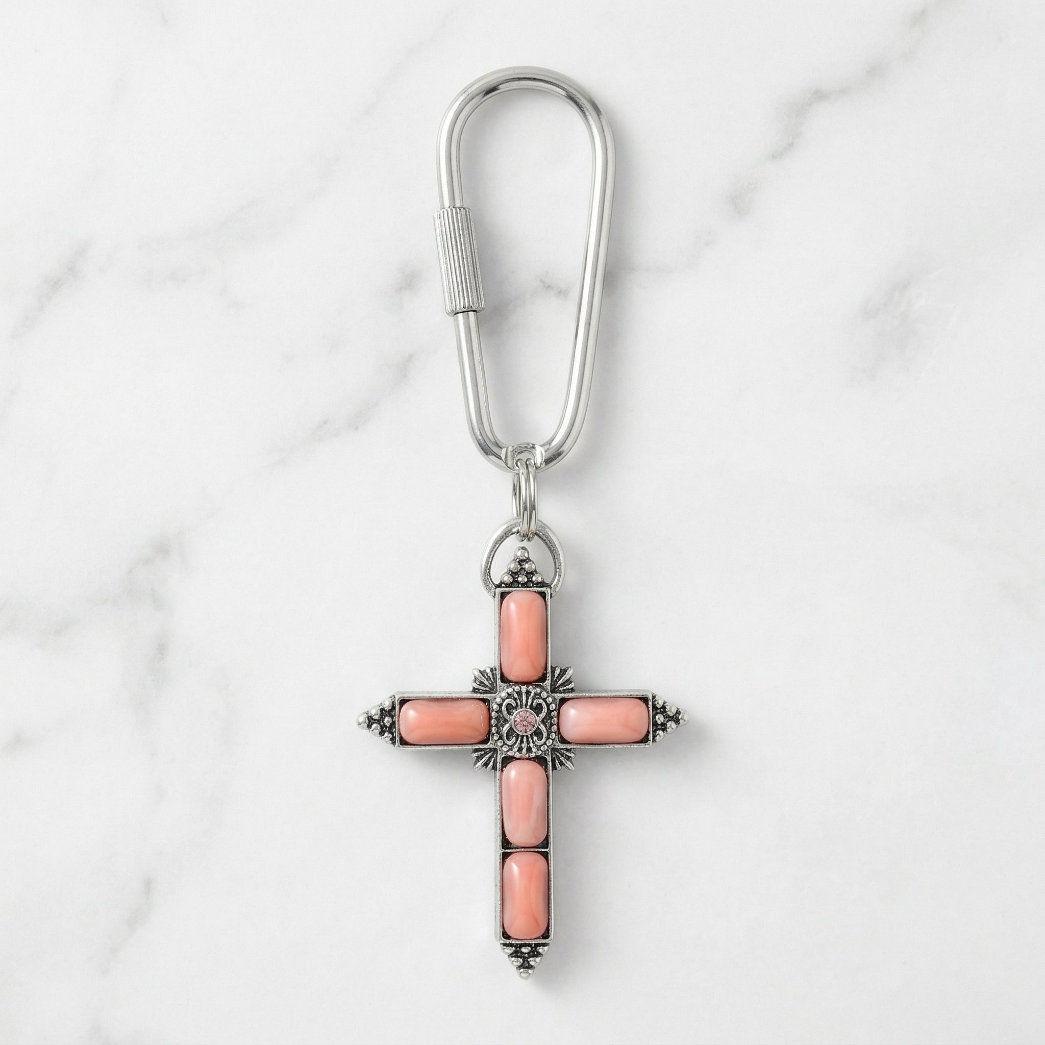 Cross-shaped keychain with pink stones on a marble background