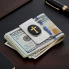 Cross designed money clip clamping a stack of US dollars on a desk.