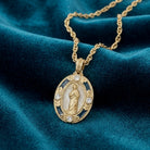 Gold necklace with a praying Mother Mary pendant on a blue fabric background