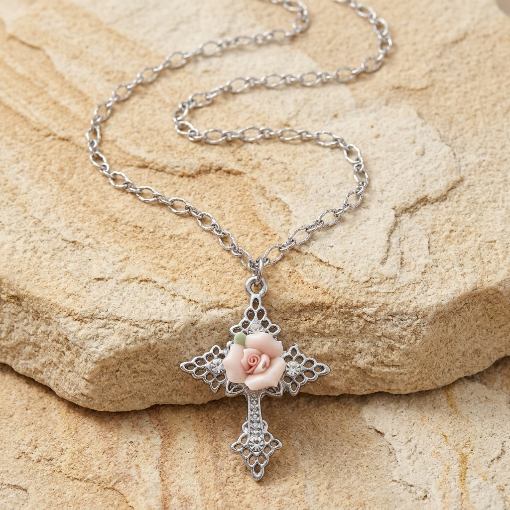 Silver necklace with a cross pendant featuring a pink rose on a stone surface