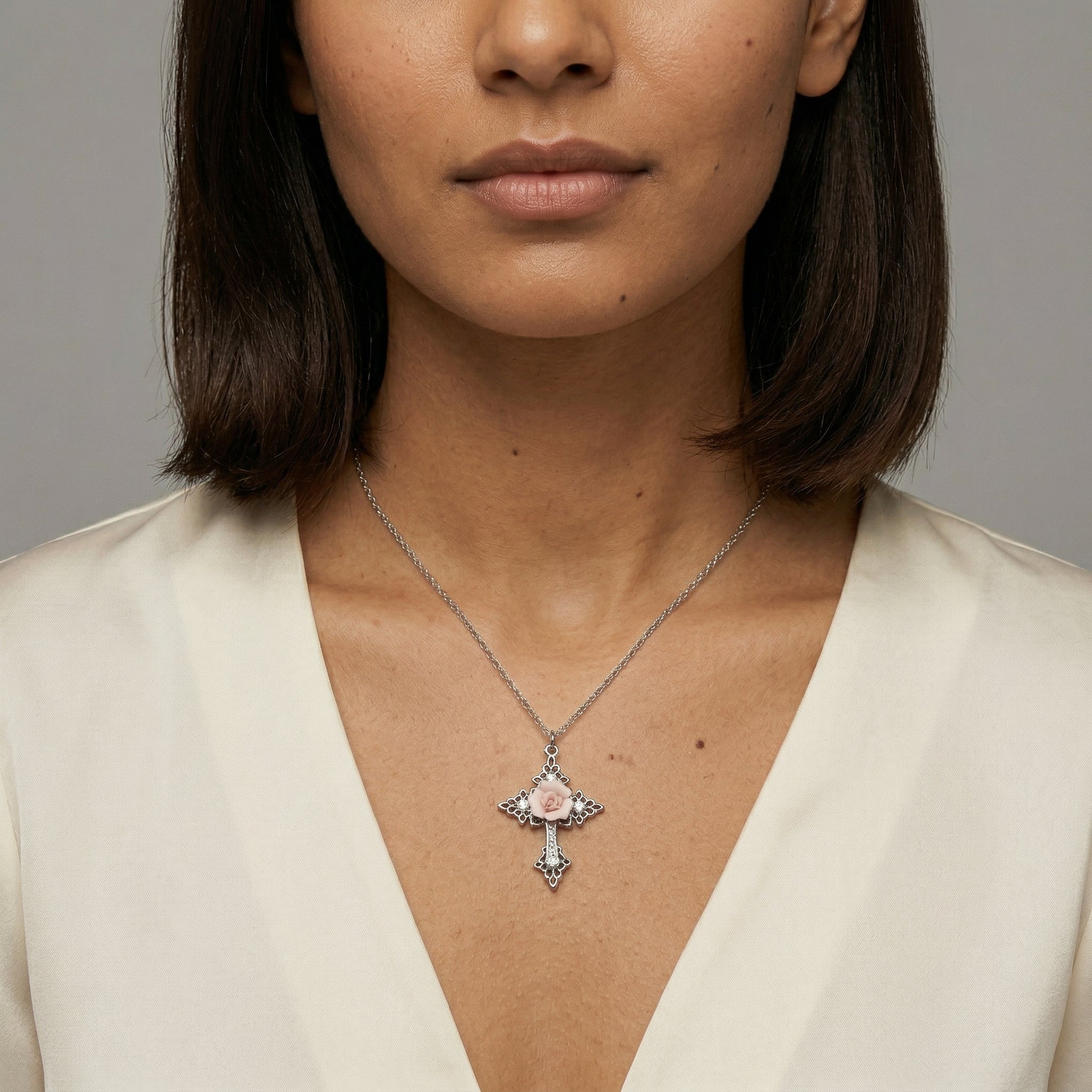 Woman wearing a necklace with a detailed cross pendant and rose design against a neutral background