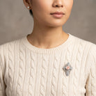 Woman in a cream sweater wearing a silver tone cross brooch with a genuine handmade porcelain rose center